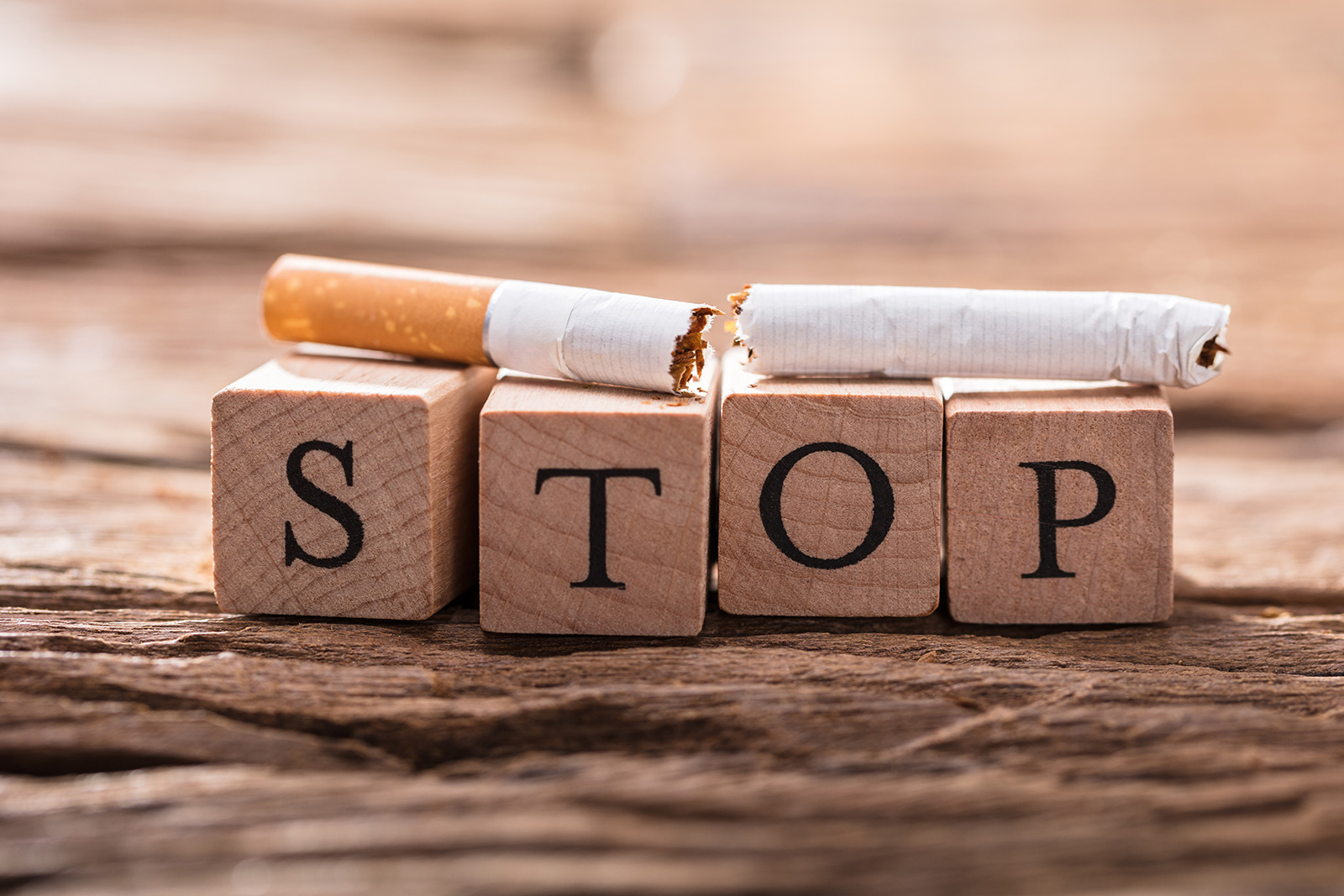 Durchgebrochene Zigarette liegt auf Würfel mit dem Schriftzug "Stop"