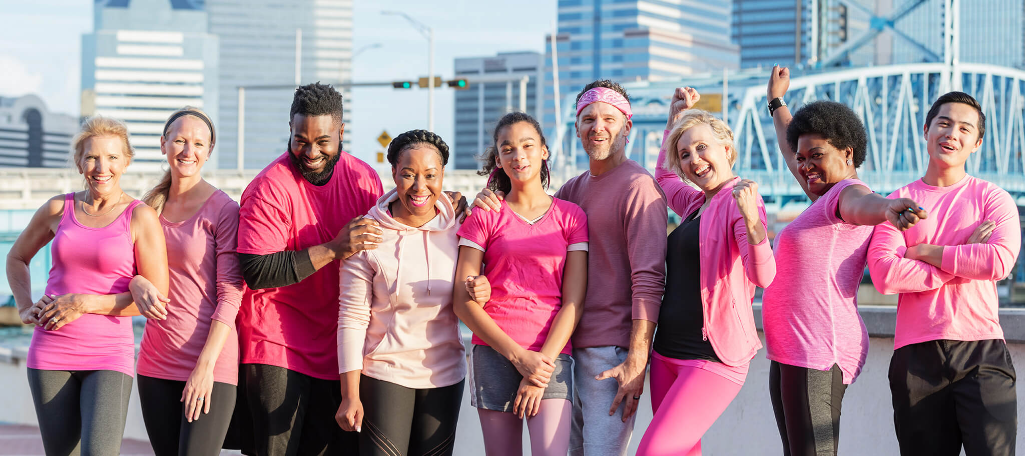 Eine multiethnische Gruppe von Männern und Frauen unterschiedlichen Alters, die zusammenstehen und rosa tragen. Sie sind draußen in einer Stadt und lächeln in die Kamera.