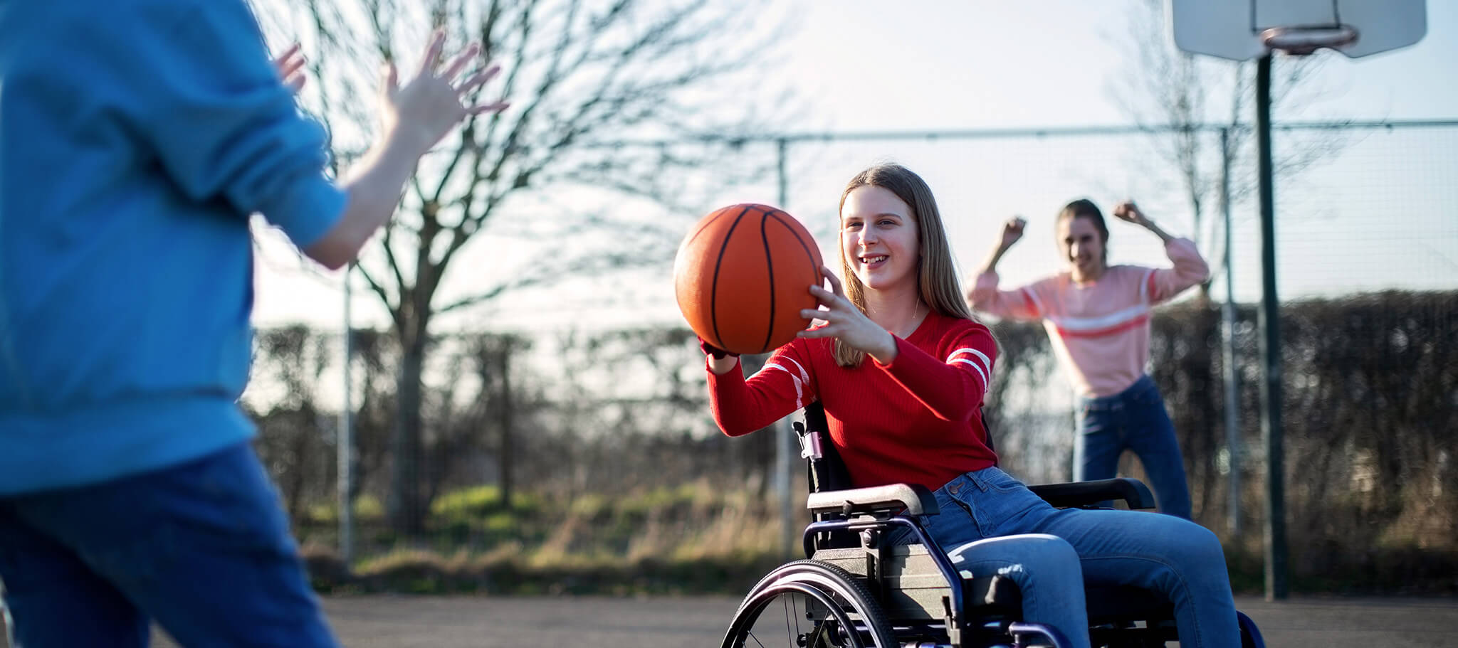 Teenager-Mädchen im Rollstuhl spielt draußen Basketball mit Freunden.