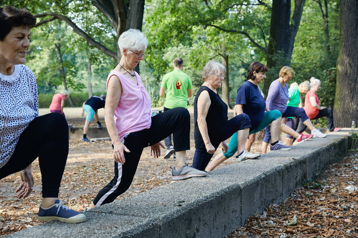 Ältere Damen machen Stretching-Übungen an einer niedrigen Mauer in einem Park