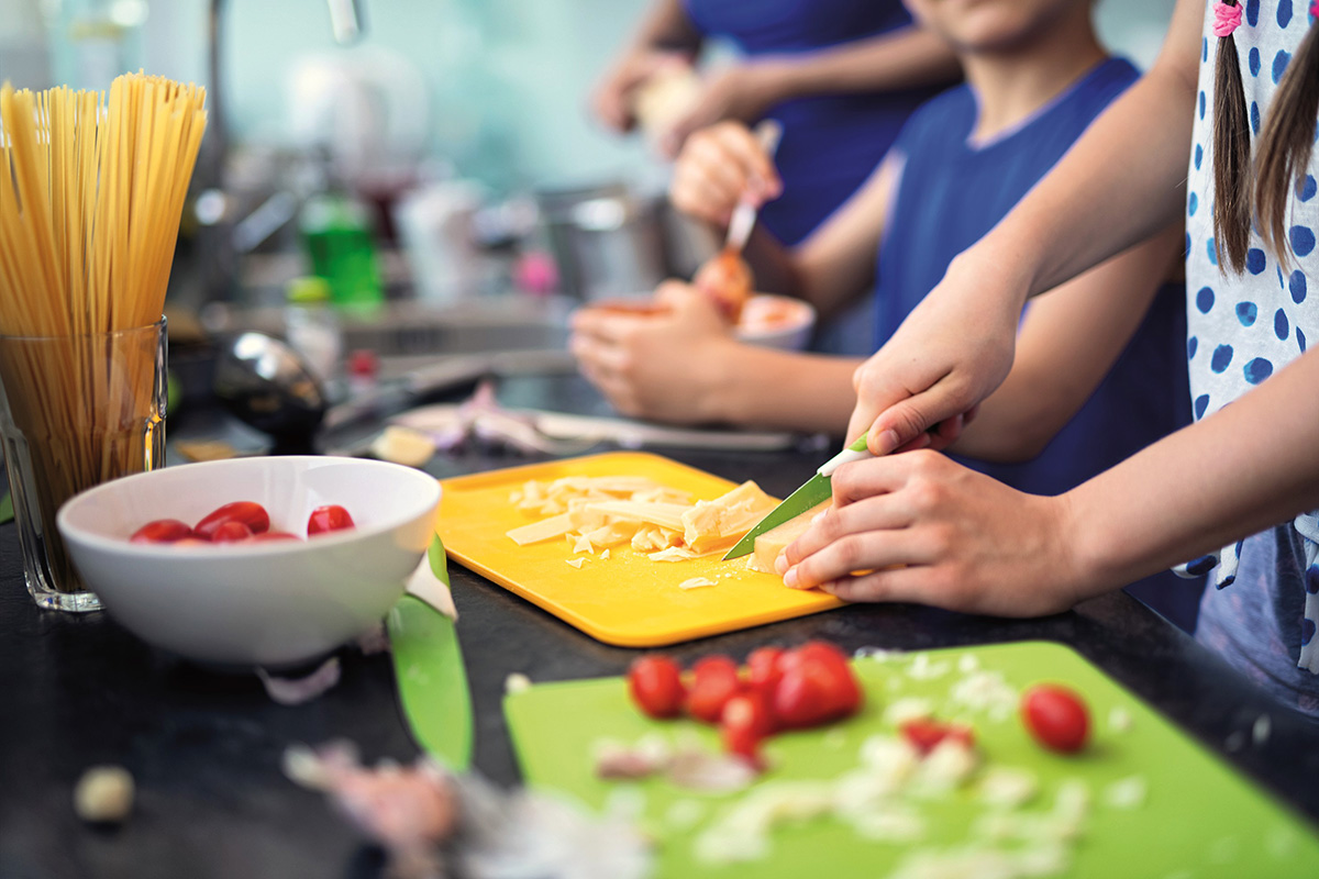 Viele Kinderhände die frische Zutaten zum Kochen schneiden