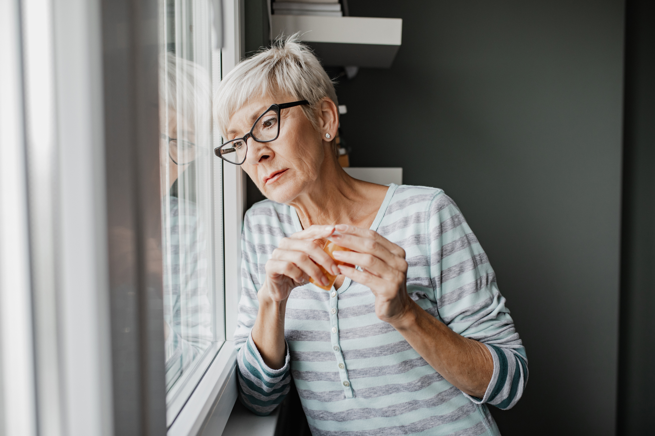 ältere Frau mit Brille die traurig aus dem Fenster schaut