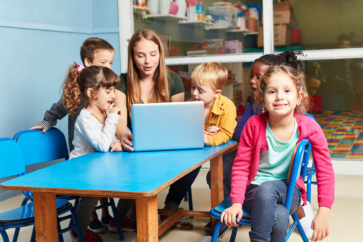 Kinder und eine Erzieherin um einen Laptop versammelt