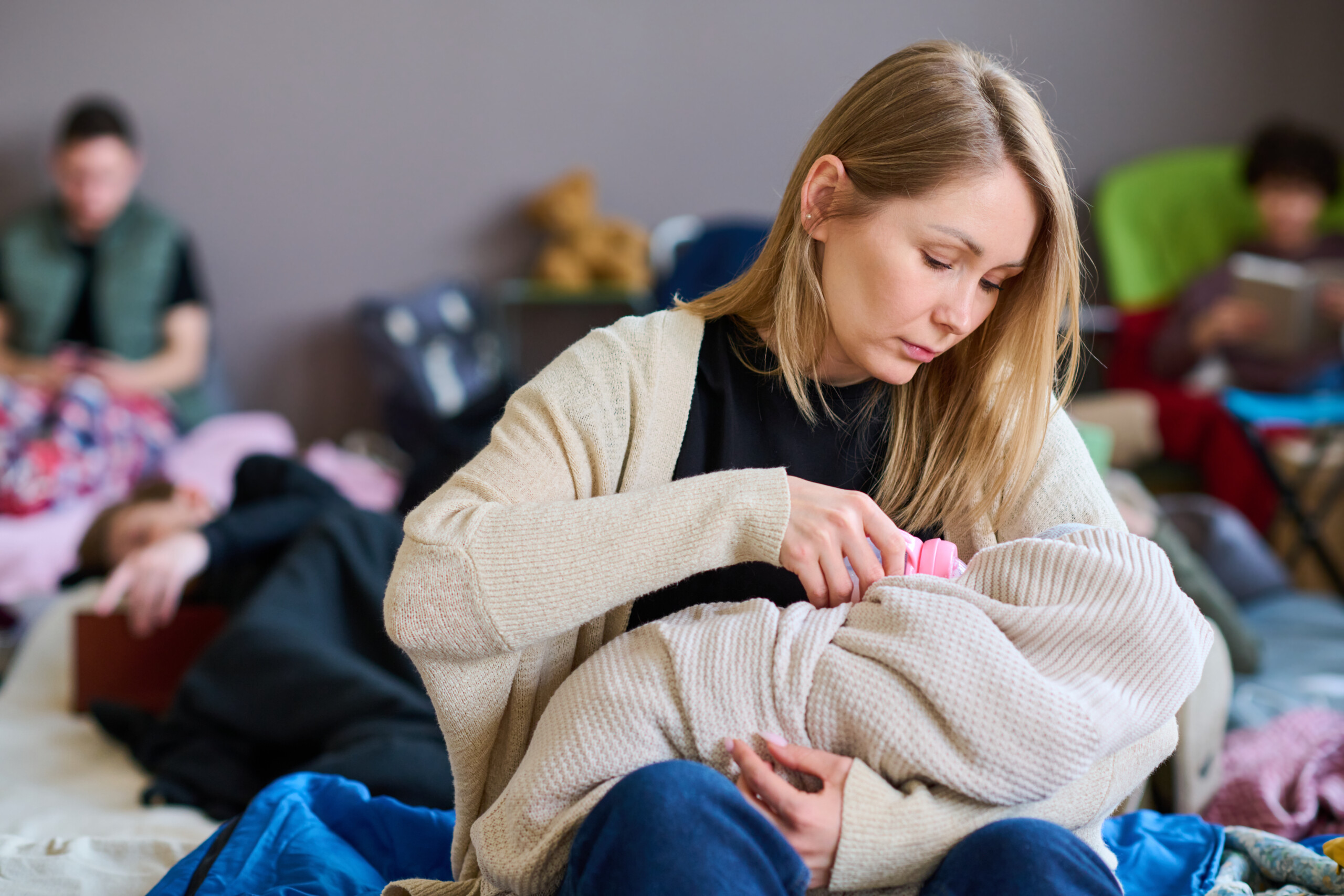 Young woman with long blond hair feeding her baby wrapped into warm plaid